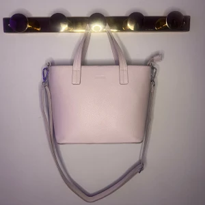 Ljusrosa/lila  axelväska - Säljer en stilren ljusrosa/lila axelväska med praktisk dragkedja och avtagbar axelrem. Väskan har två handtag och flera fack inuti för enkel organisering. Perfekt för att bära med sig det viktigaste med stil.