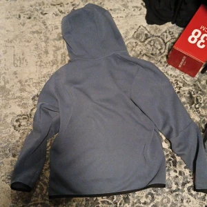 Blå huvtröja från Nike - Säljer en blå huvtröja från Nike med dragkedja framtill. Tröjan har en klassisk design med långa ärmar och en bekväm huva. Perfekt för en avslappnad stil.