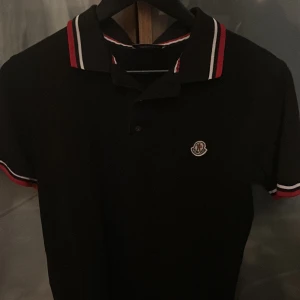 Svart pikétröja från Moncler - Säljer en stilren svart pikétröja från Moncler. Tröjan har en broderad Moncler-logga på bröstet. Perfekt för en avslappnad men ändå snygg look. Pris kan diskuteras i Dm och fråga alltid om du undrar något.