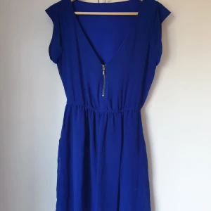 Blå klänning med dragkedja - Snygg blå klänning med v-ringning och dragkedja. Klänningen har korta ärmar och en elastisk midja för en bekväm passform. Strolek M men passar även M. Den är köpt i Spanien så vet inte vilket märke det är