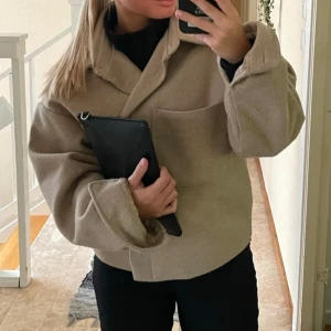 Kort kappa - Säljer denna beiga kappa från Kappahl då den inte används längre, andra bilden beskriver färgen lite bättre, kappan är använd en vår så den är lite nopprig men de går ju såklart att få bort