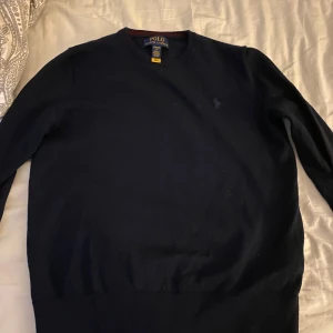 Mörkblå tröja från Polo Ralph Lauren - Säljer en stilren mörkblå tröja från Polo Ralph Lauren. Tröjan har långa ärmar och en klassisk design med rund halsringning. Passar killar mellan 11-14 år. Barn storlek large som motsvarar ungefär herrstorlek xs. Använd ett fåtal gånger. Mycket bra skick. Priset går att diskuteras