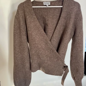 Beige omlottkofta från & Other Stories - Säljer en mysig beige omlottkofta från & Other Stories. Koftan har långa ärmar och en knytning i midjan som ger en fin passform. Perfekt för kyliga dagar och lätt att matcha med olika outfits.