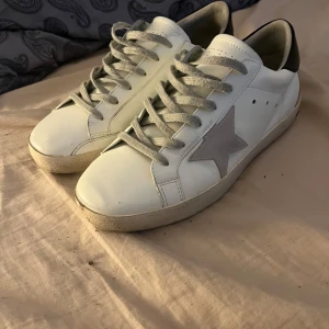 Golden goose strl 41/42 - Snygga vita sneakers med en grå stjärna på sidan och grå snörning. Skorna har en kontrasterande svart häl och perforerade detaljer på tungan. Perfekta för en stilren look.