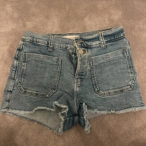 Jeansshorts från Zara - Säljer ett par coola jeansshorts från Zara. De är blå med två fickor där fram och bak och har en klassisk femficksdesign. Perfekta för en avslappnad stil.