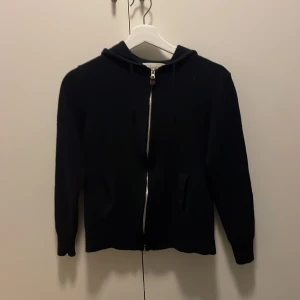 Sayless cashmere hoddie - Säljer en stilren svart hoodie med dragkedja framtill. Tröjan har långa ärmar och en praktisk huva. Perfekt för en avslappnad look. Materialet är cashmere som ger en väldigt kvalitativ känsla.