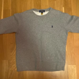 Grå tröja från Polo Ralph Lauren 10-12år - Säljer en klassisk grå tröja från Polo Ralph Lauren med det ikoniska broderade logotypen på bröstet. Tröjan har rund hals och perfekt för en avslappnad stil. Passar bra till både jeans och chinos.