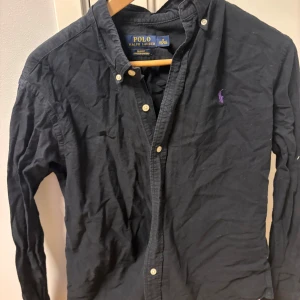 Svart skjorta från Ralph Lauren - Säljer en stilren svart skjorta från Ralph Lauren i slim fit. Skjortan har långa ärmar och knappar framtill. Den är tillverkad i stretchigt material för extra komfort. Inga defekter. Kom med bud!!