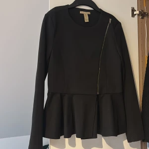 Svart kappa/blus med dragkedja - Snygg svart kappa/blus från nelly med en unik asymmetrisk dragkedja och volangdetalj i nederkant. Långärmad och i en klassisk svart färg. passar perfekt för alla tillfällen🫶