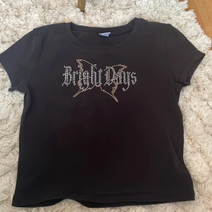 Svart t-shirt med text från Lindex - Säljer en svart t-shirt från Lindex med texten 'Bright Days' i glittriga stenar på framsidan. T-shirten har en rund halsringning och korta ärmar. Perfekt för en cool och avslappnad stil. Köpt för 140kr.