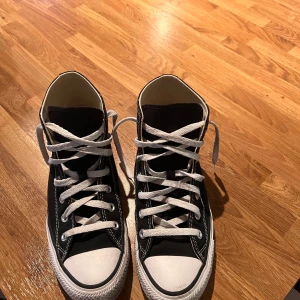 Svarta sneakers från Converse - Klassiska svarta Converse sneakers med hög snörning och vit sula. Skorna har den ikoniska logotypen på sidan och är perfekta för en avslappnad stil. De är tillverkade i slitstarkt material och har en tidlös design.