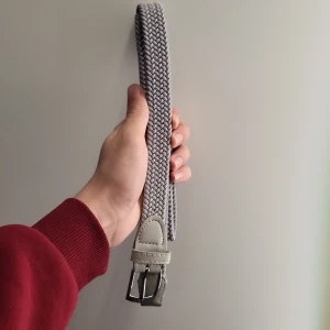 Grått onewear bälte (helt ny) - Snyggt grått flätat bälte med silverfärgat spänne. Bältet har detaljer i ljust skinn vid spännet och ändarna. Perfekt för att ge en stilren touch till din outfit.