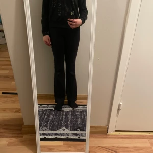 Svart hoodie med paljettdetaljer - Snygg svart hoodie med dragkedja och paljettdetaljer i form av ett skelettmönster på framsidan. Perfekt för en cool och avslappnad stil. Den har långa ärmar och en bekväm passform.