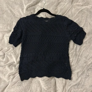 Mörkblå stickad topp - Säljer en mörkblå stickad topp med ett detaljerat mönster. Toppen har korta ärmar och en rund halsringning. Perfekt för en stilren look.