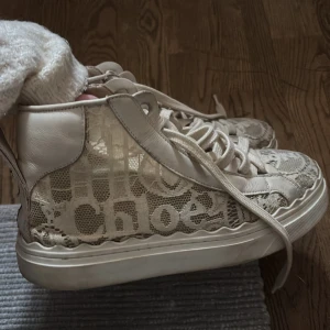 Beige sneakers med spetsdetaljer från Chloé - Snygga beige sneakers från Chloé med unika spetsdetaljer och snörning. Skorna har en högre modell och märkeslogga på hälen. Dem är i bra skick, går att rusta genom att tvätta lätt. Nypris 5200kr! Skriv vid funderingar och köp en direkt!!