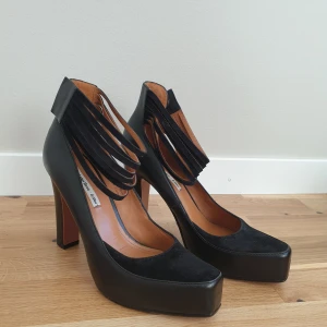 Svarta klackskor med remmar - &other stories - Eleganta svarta klackskor med flera remmar över vristen, från &other storis. Skorna har en hög klack och en spetsig tå, vilket ger en stilren och modern look. Tillverkade i skinn med en slät finish.