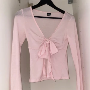 Rosa långärmad topp med knyt - Säljer en söt rosa långärmad topp från gina tricot i storlek xs. Toppen har en v-ringad design med knyt framtill som ger en feminin touch. Perfekt för både vardag och speciella tillfällen.