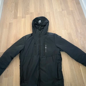 Svart jacka från Sail Racing - Säljer en svart jacka från Sail Racing i storlek medium. Jackan har en stilren design med dragkedja och flera praktiska fickor. Perfekt för kyligare väder med sin vindtäta och vattenavvisande funktion.