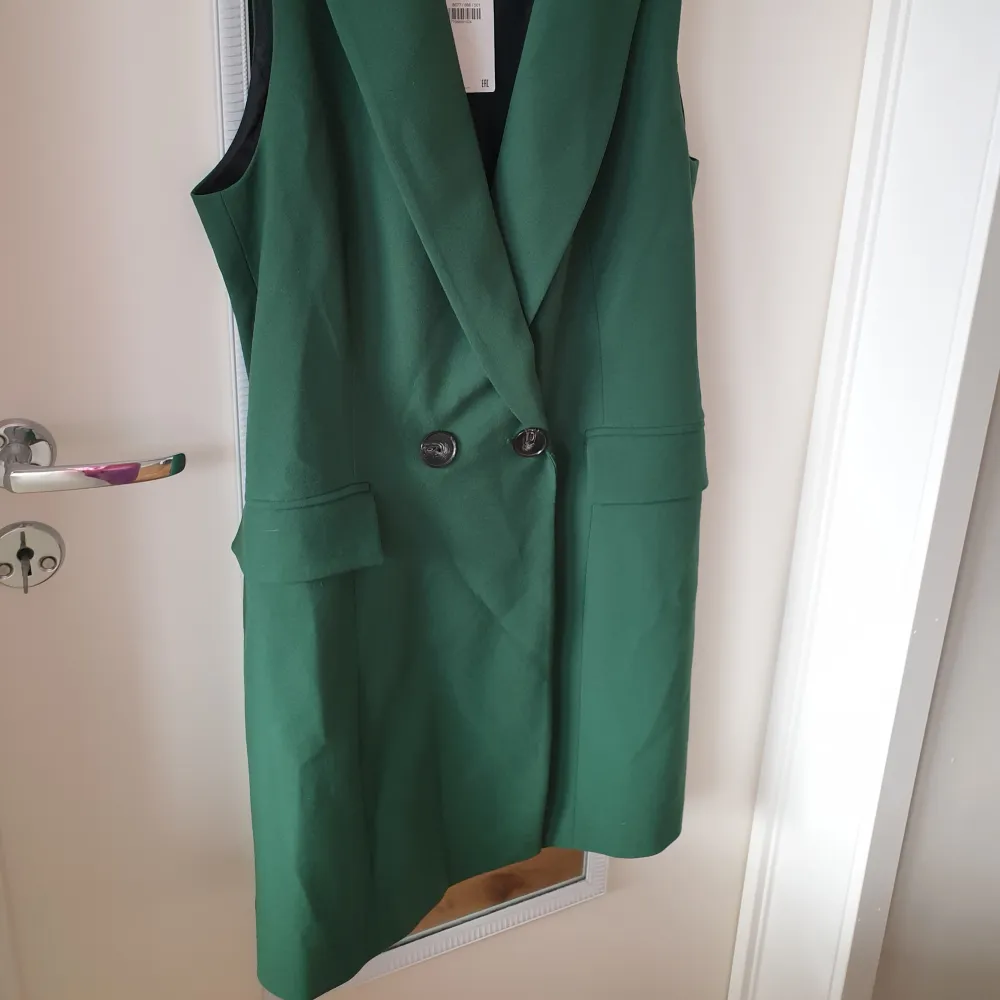 Snygg grön ärmlös klänning från Zara med dubbelknäppning framtill. Perfekt för en stilren look. Klänningen har en klassisk krage och fickdetaljer som ger en elegant touch. Ca 87cm lång. Mekot.