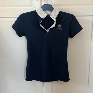 Mörkblå polotopp med vit krage ( rid tröja) - Snygg mörkblå polotopp från Kingsland med vit krage och korta ärmar. Perfekt för en stilren look. Toppen har en liten broderad logga på bröstet.