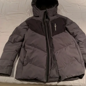 Grå vinter jacka från Sail Racing - Snygg grå vinterjacka från Sail Racing med svart detalj på bröstet . Jackan har en används ett par gångar men är fortfarande i riktigt bra skick.