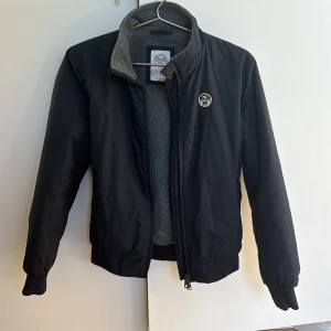 Northsailsjacka - En fräsch blå North Sailsjacka i st S (160-170kcm) för endast 349kr. En dragkedjebit lossnat men funkar fortfarande att använda dragkedjan.  Nypris 1300kr