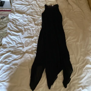 Svart ärmlös klänning - Säljer en elegant svart klänning som är ärmlös och har en asymmetrisk nederdel. Perfekt för festliga tillfällen! Klänningen har en fin spetsdetalj upptill och är gjord i ett lätt och flödande material.