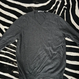 Grå v-ringad tröja - Säljer en stilren Uniqlo grå tröja med v-ringning. Perfekt för både vardag och lite finare tillfällen. Tröjan har långa ärmar och är i ett mjukt material som känns skönt mot huden. Passar bra till höst och vinter!