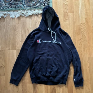 Svart hoodie från Champion - Säljer en svart hoodie från Champion i storlek medium. Den har en klassisk Champion-logga på bröstet och en mindre logga på ärmen.