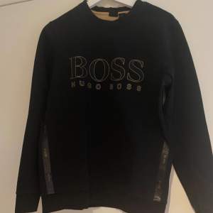 Säljer en snygg svart tröja från Hugo Boss med deras ikoniska logga tryckt på framsidan. Tröjan har långa ärmar och en stilren design som passar perfekt till både vardag och fest. Den är i bra skick och redo för en ny ägare!