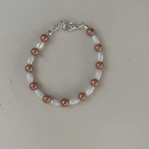 Pärlarmband med vita och bruna pärlor - Snyggt armband med vita och bruna pärlor. Perfekt för att ge en elegant touch till din outfit. Armbandet har en enkel och säker låsning i silverfärg.