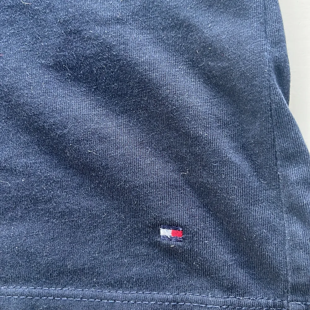 Säljer en snygg mörkblå t-shirt från Tommy Hilfiger i storlek XS. Den har ett klassiskt tryck med märkesnamnet på framsidan och en liten logga nedtill. Perfekt för en casual look!. T-shirts.