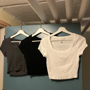 Tre ribbade toppar från H&M - Säljer tre snygga ribbade toppar från H&M i storlek M. De kommer i tre olika färger: vit, svart och grå. Perfekta för vardagsbruk eller att styla upp för en fest. Topparna har en tight passform och korta ärmar.