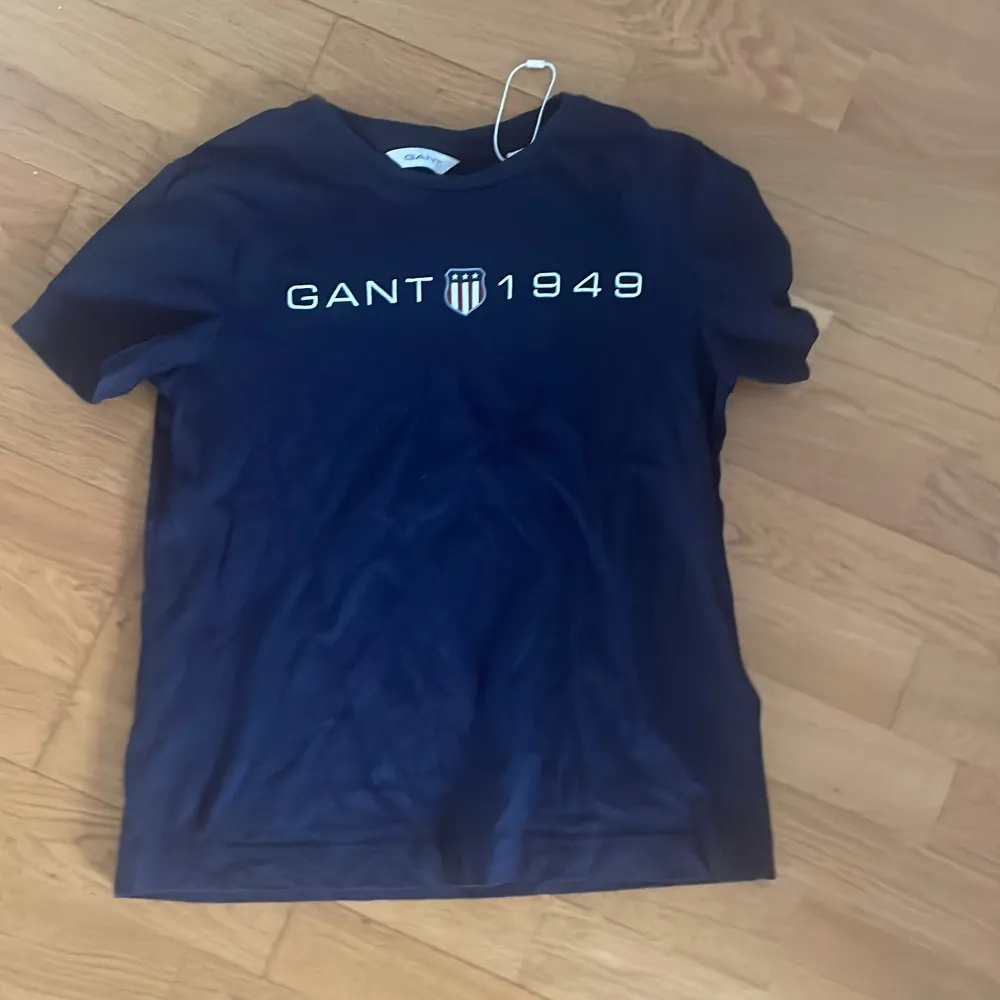 Snygg mörkblå t-shirt från Gant med tryck 'GANT 1949' på framsidan. Perfekt för en avslappnad stil. Klassisk rund hals och korta ärmar.. T-paidat.