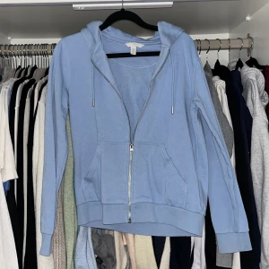 Blå hoodie från H&M - Säljer en snygg blå hoodie från H&M med dragkedja och justerbar huva. Perfekt för en avslappnad stil. Den har långa ärmar och praktiska fickor framtill. Passar perfekt för kyliga dagar.