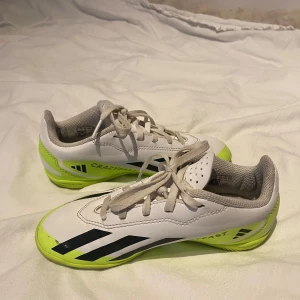 Vita och limegröna fotbollsskor från Adidas - Snygga fotbollsskor från Adidas i vitt med limegröna och svarta detaljer. Skorna har snörning och en sportig design. Perfekta för fotbollsplanen!