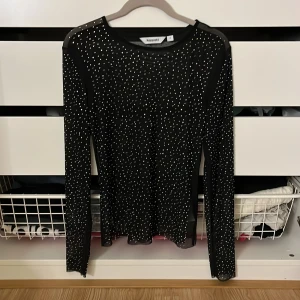 Svart glittrig topp från Kappahl - Snygg svart topp från Kappahl med glittriga detaljer. Den har långa ärmar och är perfekt för en kväll ute. Toppen är i ett stretchigt material som ger en bekväm passform.