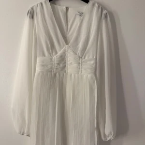 Vit Studentklänning Bubbleroom - Elegant vit  studentklänning från Bubbleroom med v-ringad design och långa ärmar. Klänningen har en smickrande rynkad detalj vid midjan och ett luftigt, plisserat kjolparti. Perfekt för speciella tillfällen, samt studenten. Helt ny oanvänd, Studentklänning ifrån Bubbleroom!   Köpte ett par andra klänningar, och nu står denna bara i garderoben. Alla lappar är kvar! Nypris: 799kr Säljer för 499kr Storlek: XXS Super fin Skön och luftig o perfekt inför studenten :) Pris går art diskuteras