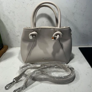 Beige handväska  - Snygg och helt oanvänd beige handväska med stilren design. Väskan har två handtag och kommer med en avtagbar axelrem. Skriv privat för fler bilder💗