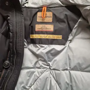 Säljer en svart dunjacka från Parajumpers i storlek XL. Jackan har en quiltad design med dragkedja och knappar framtill. Den har långa ärmar och flera praktiska fickor. Perfekt för kalla dagar.