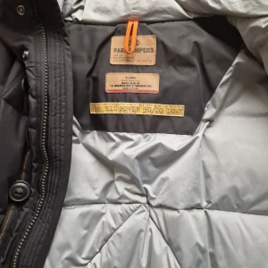 Svart dunjacka från Parajumpers - Säljer en svart dunjacka från Parajumpers i storlek XL. Jackan har en quiltad design med dragkedja och knappar framtill. Den har långa ärmar och flera praktiska fickor. Perfekt för kalla dagar.