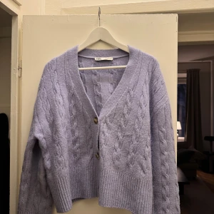 Ljuslila stickad kofta från Zara - Mysig ljuslila stickad kofta från Zara med kabelstickat mönster. Koftan har en v-ringning och stängs med tre knappar framtill. Perfekt för kyliga dagar!
