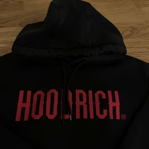 Svart hoodie från Hoodrich - Snygg svart hoodie från Hoodrich med röd text på bröstet. Perfekt för en casual look med en skön passform och justerbar huva.