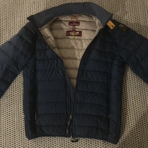 Mörkblå dunjacka från Parajumpers - Säljer en snygg mörkblå dunjacka från Parajumpers. Jackan har en quiltad design med dragkedja framtill och en broderad logga på ärmen. Perfekt för kyliga dagar med sin varma och stilrena look. I nyskick, NYPRIS 5000kr