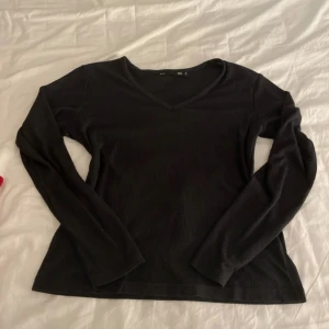 Svart v-ringad tröja från 157 - Säljer en stilren svart ribbad tröja från 157. Tröjan har en v-ringad hals och långa ärmar, perfekt för en enkel och bekväm look. 
