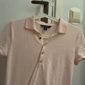 Säljer en stilren ljusrosa pikétröja från Ralph Lauren. Tröjan har korta ärmar och en klassisk krage med knappar framtill. Perfekt för en avslappnad och snygg look köpt från Ralp louren i somras pris kan diskuteras!.