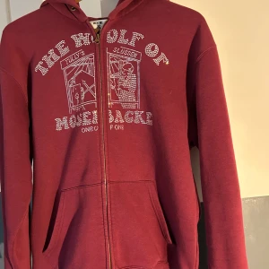 Vinröd hoodie från One of One - Säljer en snygg röd hoodie från One of One. Tröjan har en dragkedja och en bekväm passform med långa ärmar. Perfekt för att ge lite extra stil till din vardagslook.