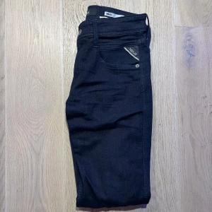 Svarta jeansbyxor från Replay - Snygga svarta jeansbyxor från Replay i modellen Anbass. De har en slim fit passform och är tillverkade i ett stretchigt material för extra komfort. Klassisk design med fem fickor och knappgylf.