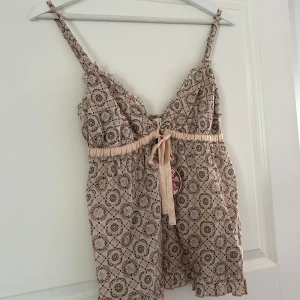 Mönstrad linne från Odd Molly - Säljer en söt mönstrad topp från Odd Molly i beige med detaljer i rosa och svart. Den har smala justerbara axelband och en knytrosett framtill. Perfekt för varma dagar! Toppen är i nyskick inköpt på oddmolly på rea för 417kr (ord pris 695kr). Säljer för 200kr! Har endast prövat toppen 1 gång, vid frågor och funderingar hör av er. Jag svarar så fort jag kan!🩷