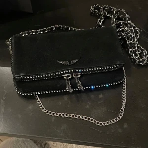 Svart axelväska från Zadig & Voltaire - Snygg svart axelväska i mocka från Zadig & Voltaire och snygga deltljer med stenar. Storlek ”nano”. Den är använd fåtal gånger och är i fint skick , som på bilderna. Materialet är mocka. Dustbag medföljer 